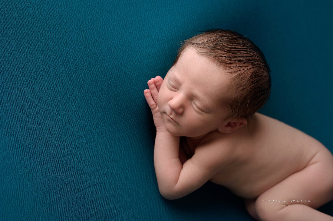 newborn baby in blue lying on his side